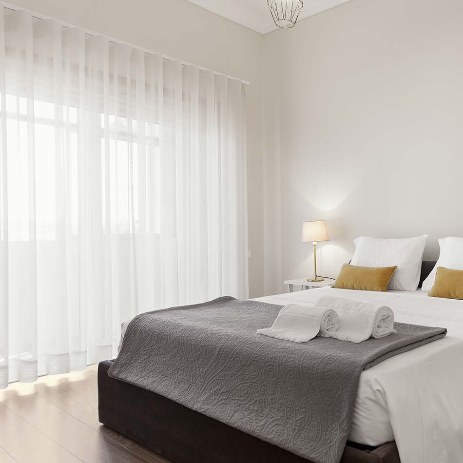 Dormitorio con cortinas translúcidas blancas cubriendo el ventanal