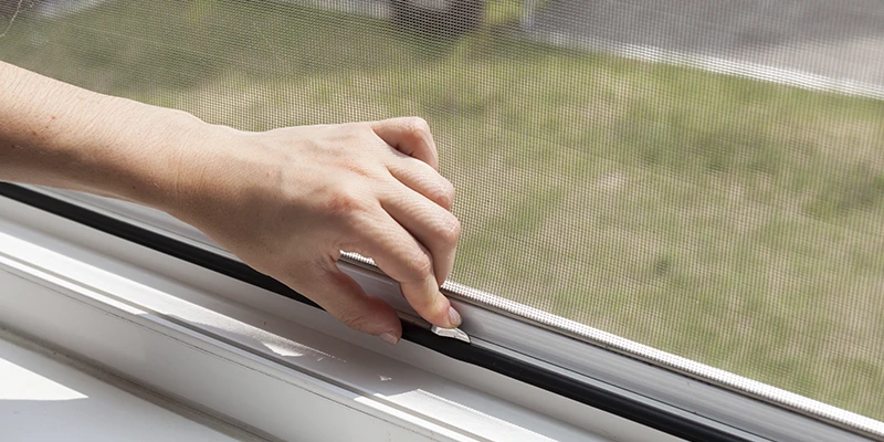 Persona abriendo una pantalla de ventana con un mango negro, mostrando la importancia de los mosquiteros en el hogar.