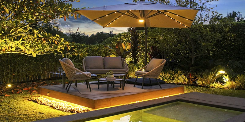 Parasol iluminado junto a la piscina en un jardín al atardecer