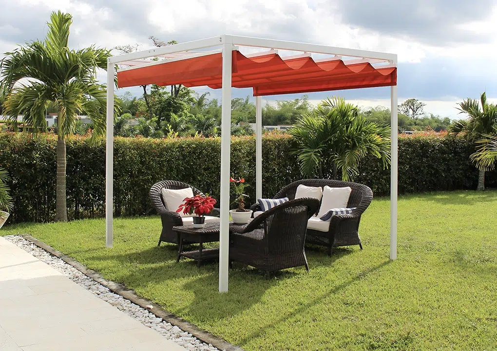 Pérgola Romana en color rojo cubriendo una sala en el exterior en una zona con pasto y naturaleza