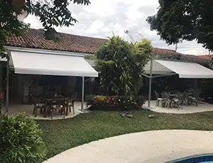 Dos toldos de doble proyección desplegados en color blanco, cubriendo unos comedores de exteriores en una casa campestre