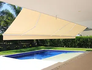 Toldo de brazos extensibles en color beige, desplegado sobre el área de una piscina de una finca campestre