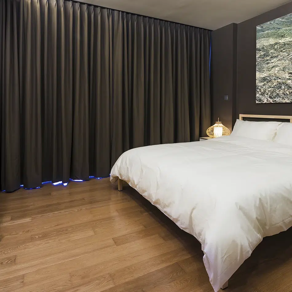 Dormitorio moderno con cortinas blackout oscuras completamente cerradas, creando un ambiente cálido y oscuro ideal para el descanso.