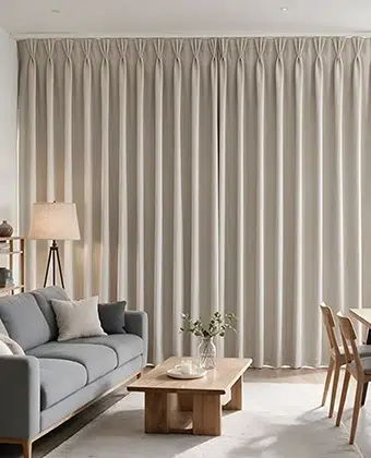 Cortinas Tripleat en tela beige con pliegues pellizcados, cubriendo un ventanal de piso a techo en una sala