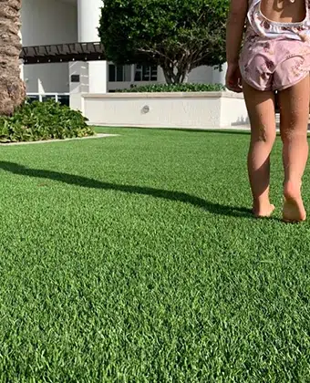 Grama artificial verde en el jardín de una casa, con una niña caminando descalza