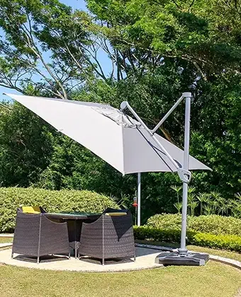 Sombrilla Cadiz blanca sobre un comedor exterior de fibra oscura, rodeada de jardín
