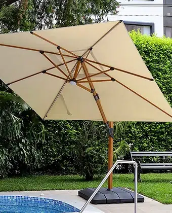 Sombrilla Kiosk Wood beige con mástil color madera junto a una piscina de mosaico azul
