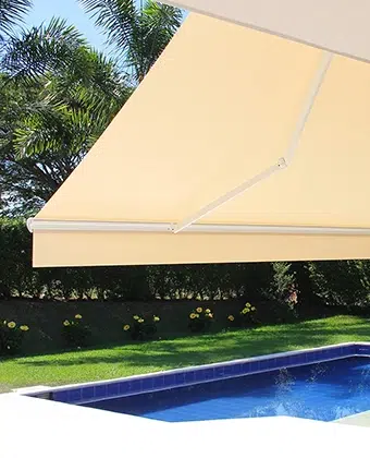 Toldo de brazos extensibles en tela beige desplegado sobre una zona de piscina con jardín
