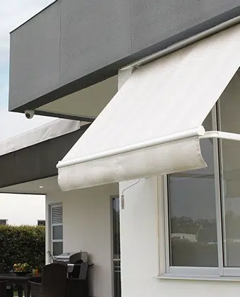 Toldo de brazos fijos en tela clara instalado sobre la ventana de una casa moderna