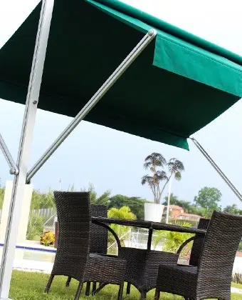 Toldo de doble proyección en tela verde sobre un comedor exterior con sillas de fibra